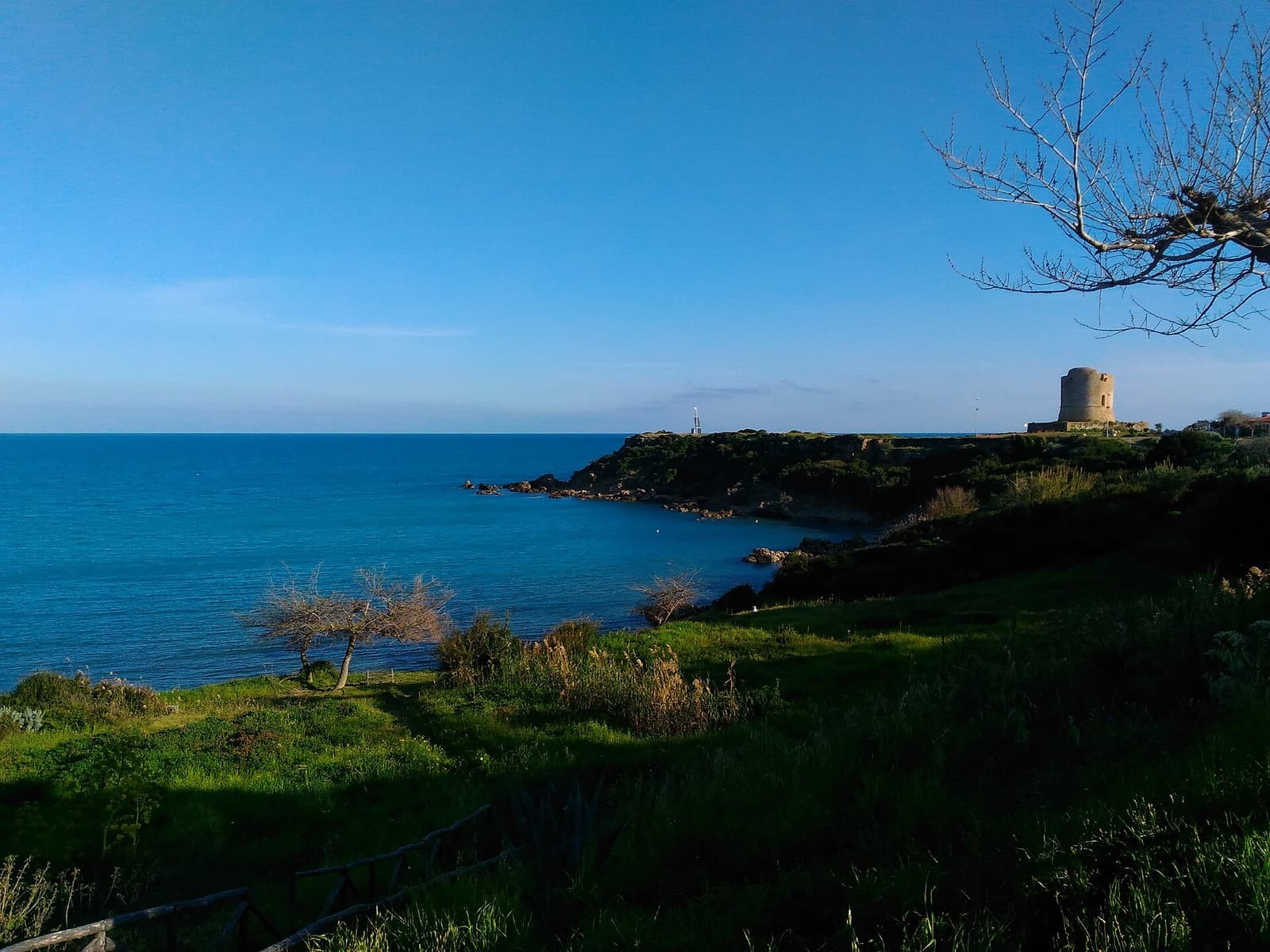 A coastal watchtower on a low green headland above the blue sea at Capo Rizzuto